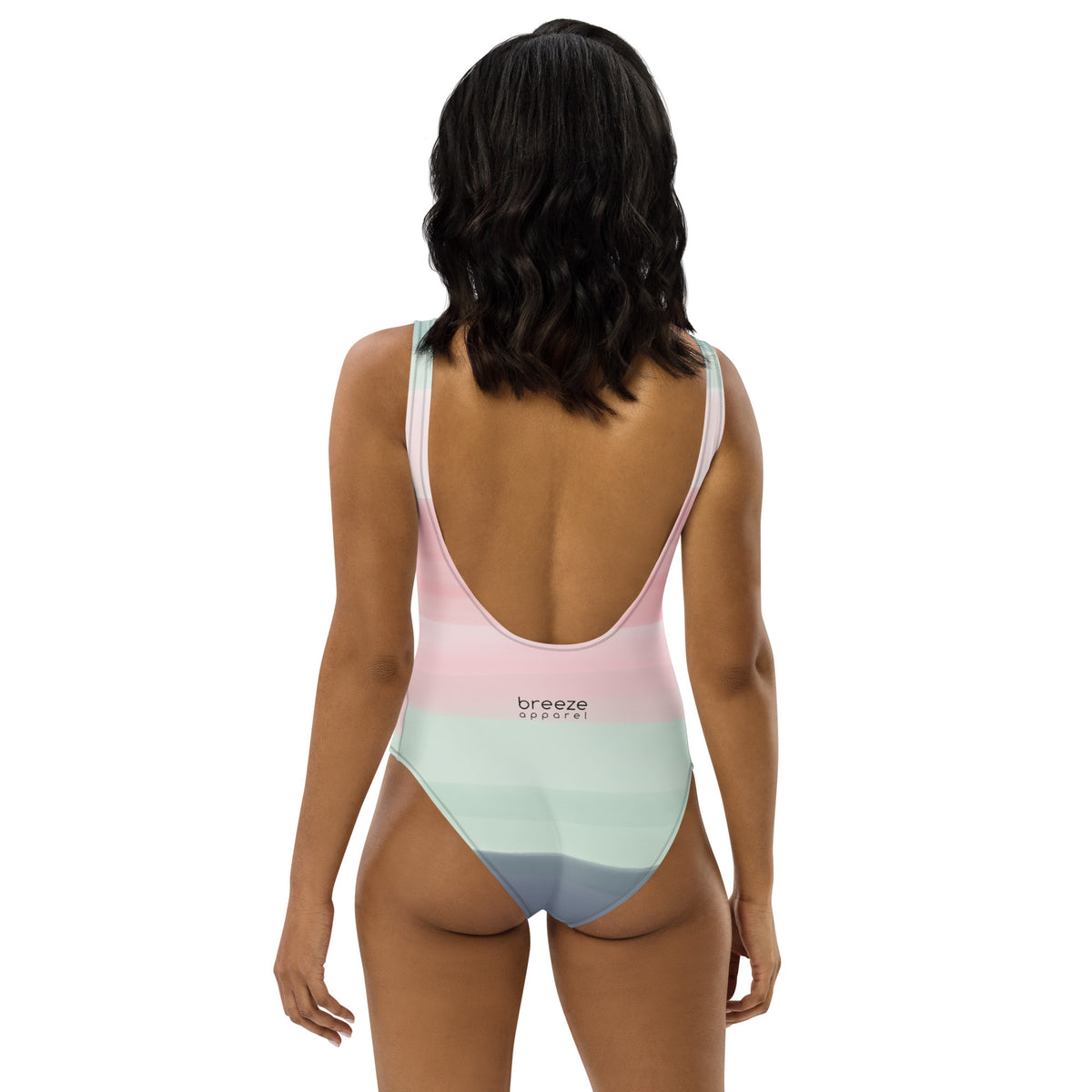 Rear view of woman wearing a one-piece swimsuit with a pink, pastel-green, and gray design that resembles watercolor.