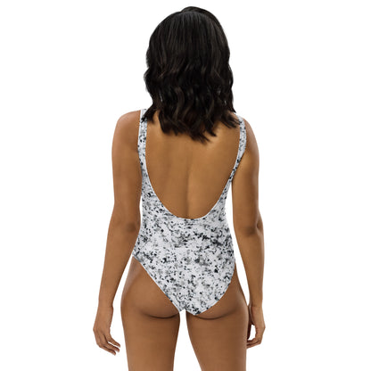 Woman wearing one-piece swimsuit with pattern of black splotches set on a white background.