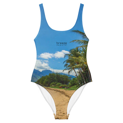 One-piece swimsuit with a coastline depicted on it. There is a clear sky, palm trees, mountains, and a beach depicted.