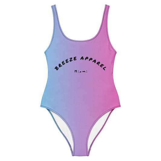 Women's one-piece swimsuit with a light-blue-to-pink design and a black 'Breeze Apparel Miami' word logo across the chest.