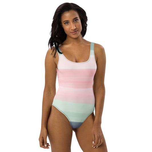 Woman wearing a one-piece swimsuit with a pink, pastel-green, and gray design that resembles watercolor.