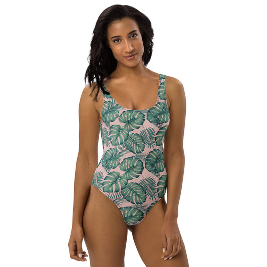 Woman wearing one-piece swimsuit with a design of palm leaves set on a pink background.