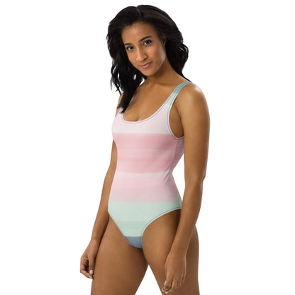 Woman wearing a one-piece swimsuit with a pink, pastel-green, and gray design that resembles watercolor.