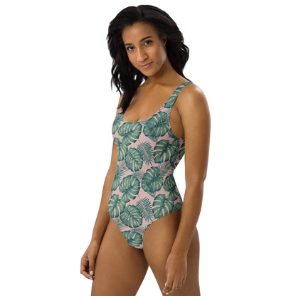 Woman wearing one-piece swimsuit with a design of palm leaves set on a pink background.