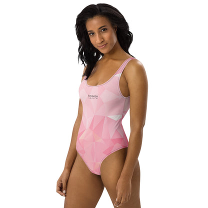 Woman wearing one-piece swimsuit with all-over, pink geometric pattern. 'Breeze apparel' is in small, black text on chest.