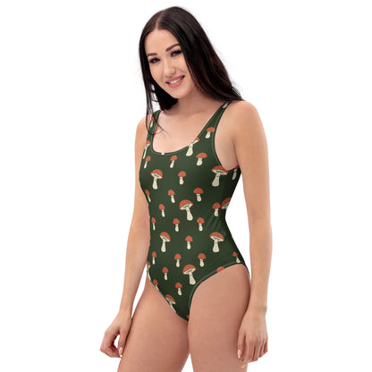 Woman wearing one-piece swimsuit with pattern of mushrooms set on green background.