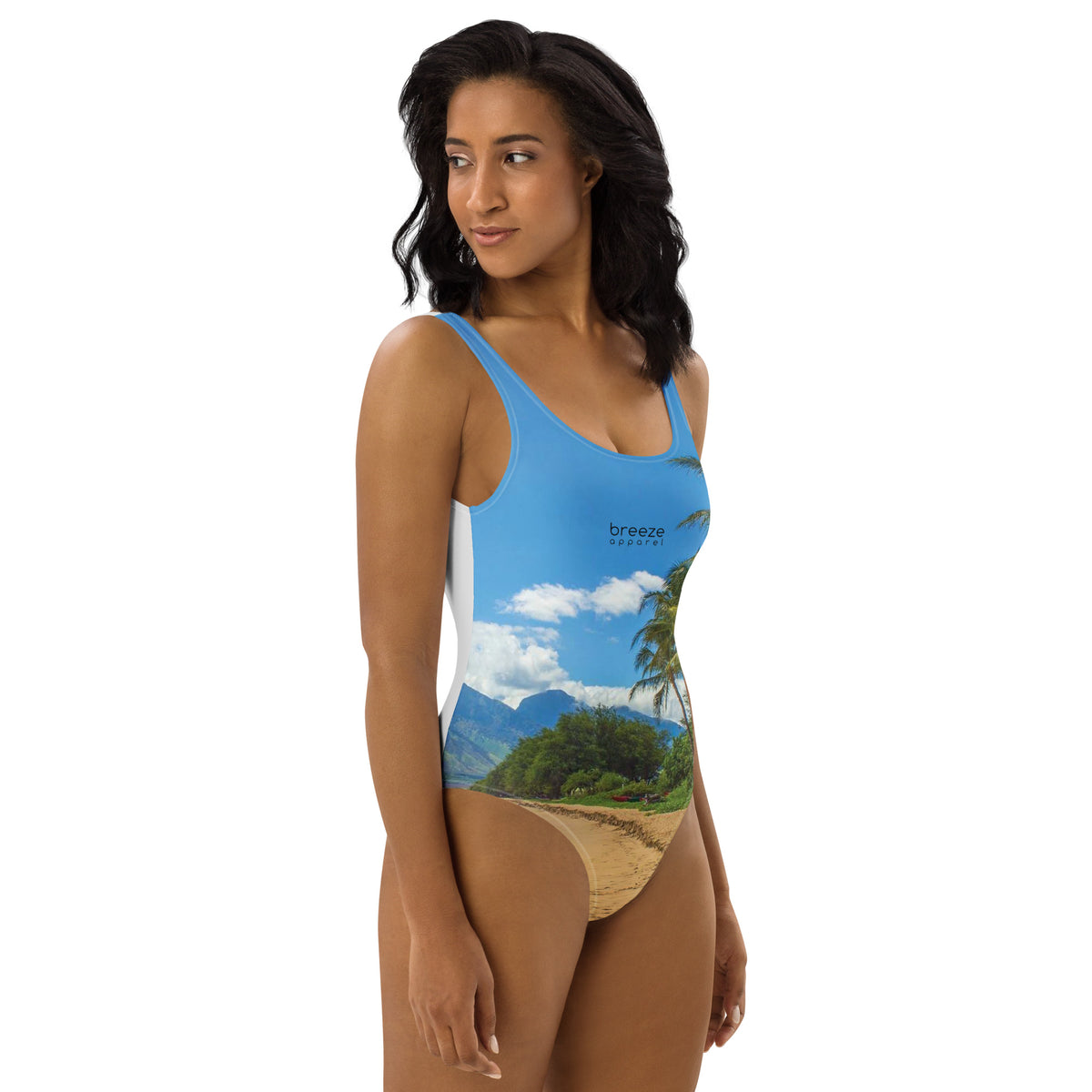 Woman wearing one-piece swimsuit with a coastline depicted on it. There is a clear sky, palm trees, mountains, and a beach depicted.