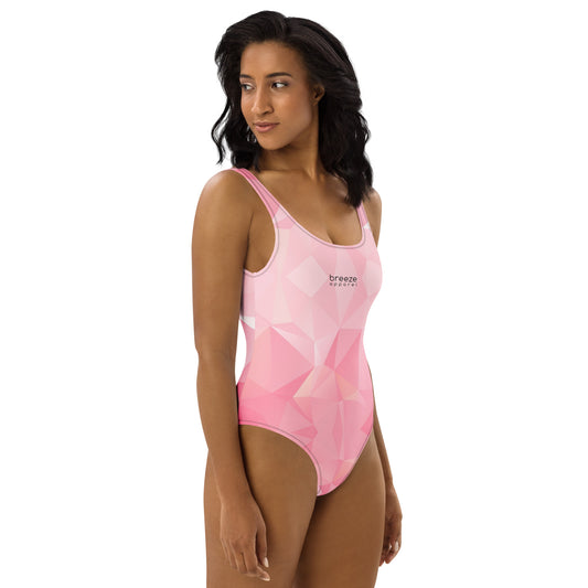 Woman wearing one-piece swimsuit with all-over, pink geometric pattern. 'Breeze apparel' is in small, black text on chest.