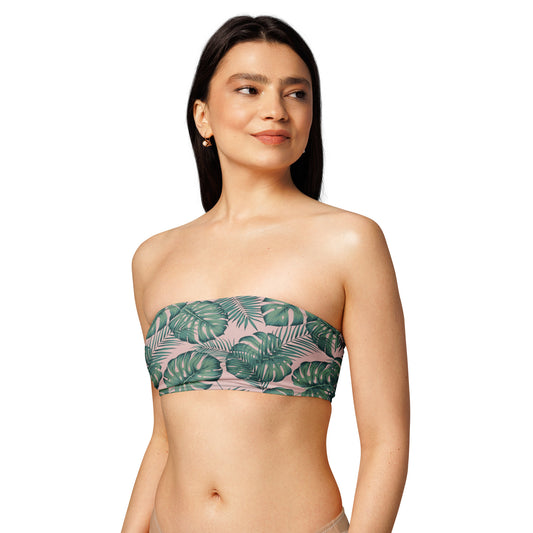 Woman wearing bandeau bikini top with design of green palm leaves set on a pink background.