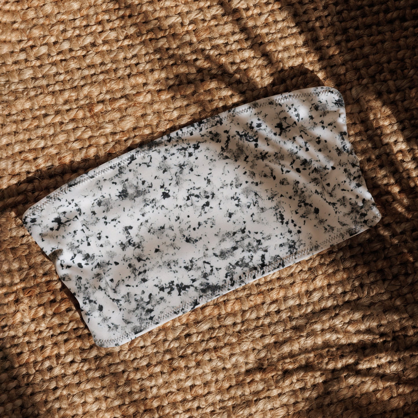 Bandeau bikini top that has a pattern of black splotches set on a white background, laying in sunlight.
