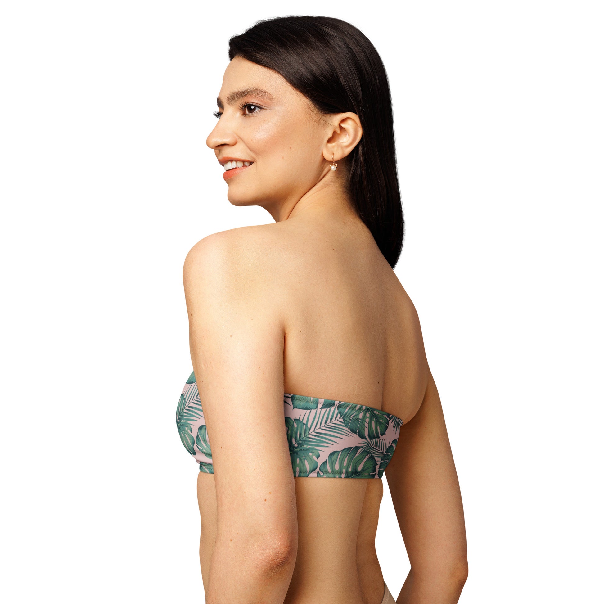 Rear view of woman wearing bandeau bikini top with design of green palm leaves set on a pink background.