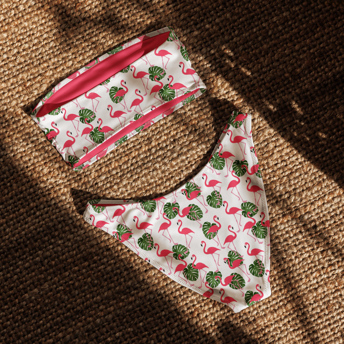 Back of white bandeau bikini with all-over flamingos design, laying in sunlight.