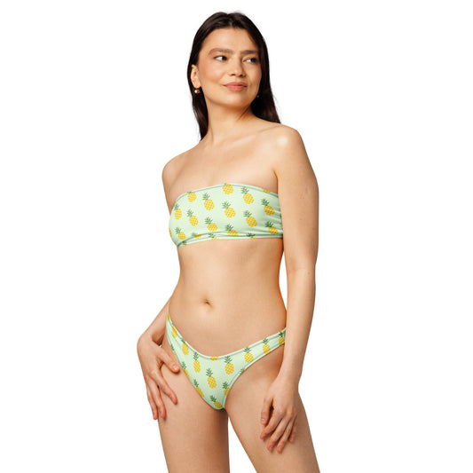 Woman wearing bandeau bikini with an all-over pineapple design set on a light-green background.