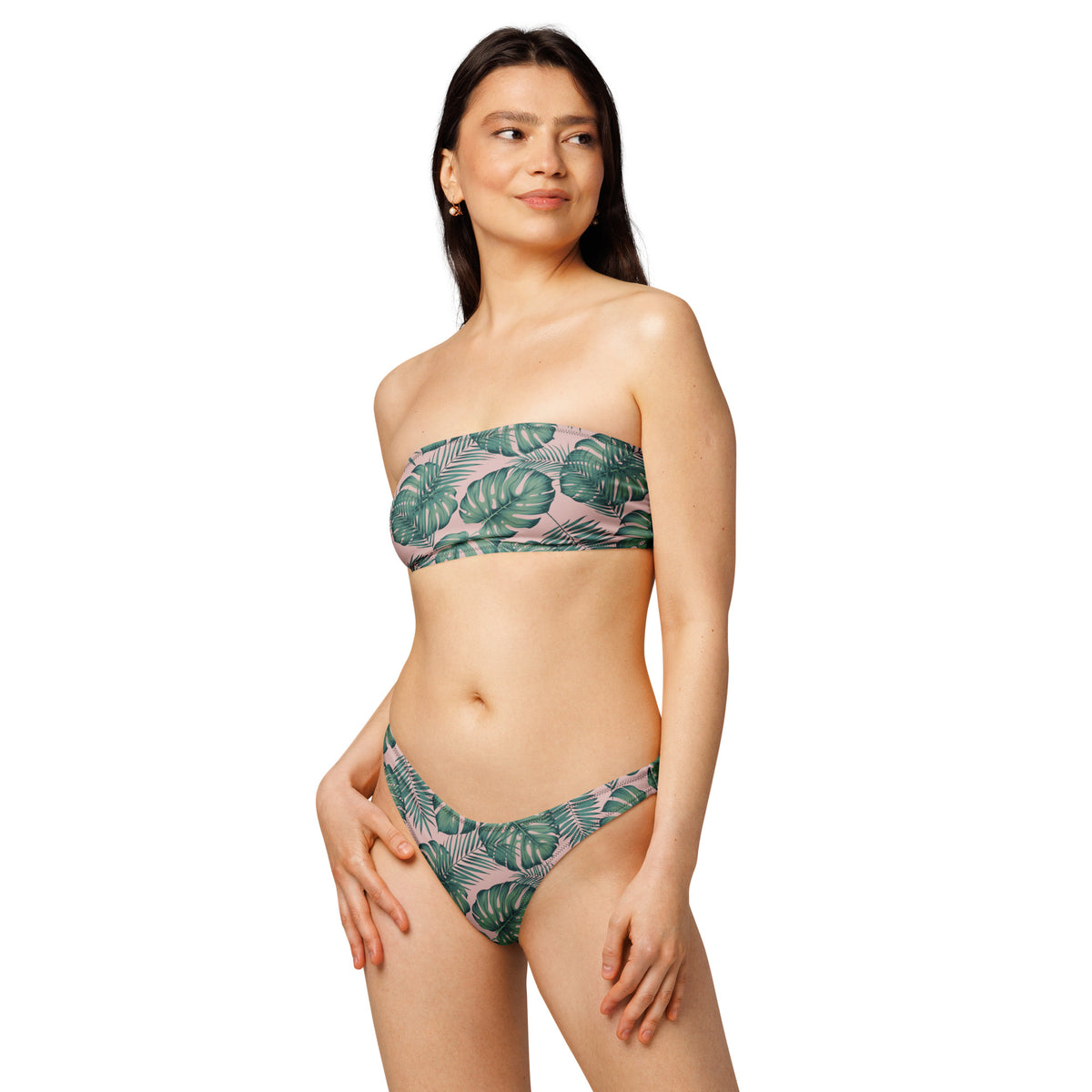 Woman wearing bandeau bikini with design of green palm leaves set on a pink background.
