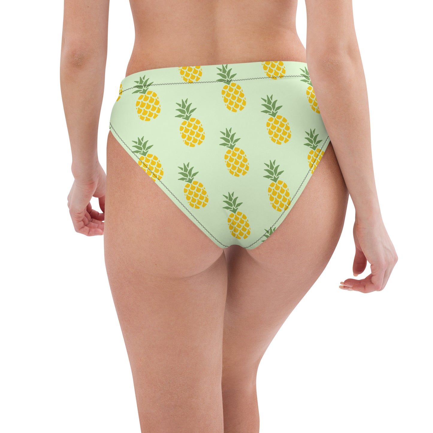 Rear view of woman wearing bikini bottom with pineapple pattern set on a light-green background.