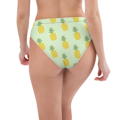 Rear view of woman wearing bikini bottom with pineapple pattern set on a light-green background.