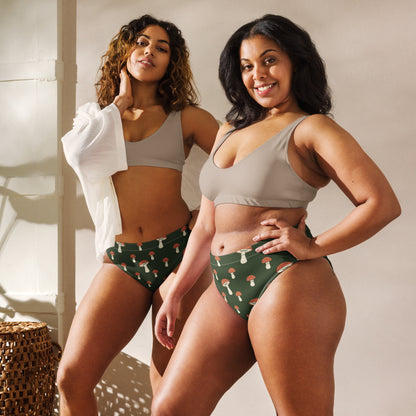 Two women, each wearing bikini bottom with pattern of mushrooms set on a green background.