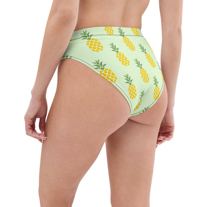 Rear view of woman wearing bikini bottom with pineapple pattern set on a light-green background.