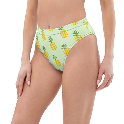 Woman wearing bikini bottom with pineapple pattern set on a light-green background.
