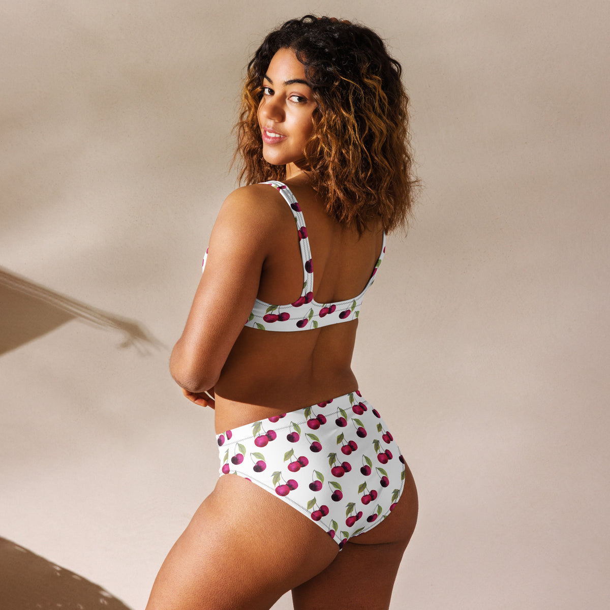 Rear view of woman wearing bikini with all-over cherry pattern set on a white background.