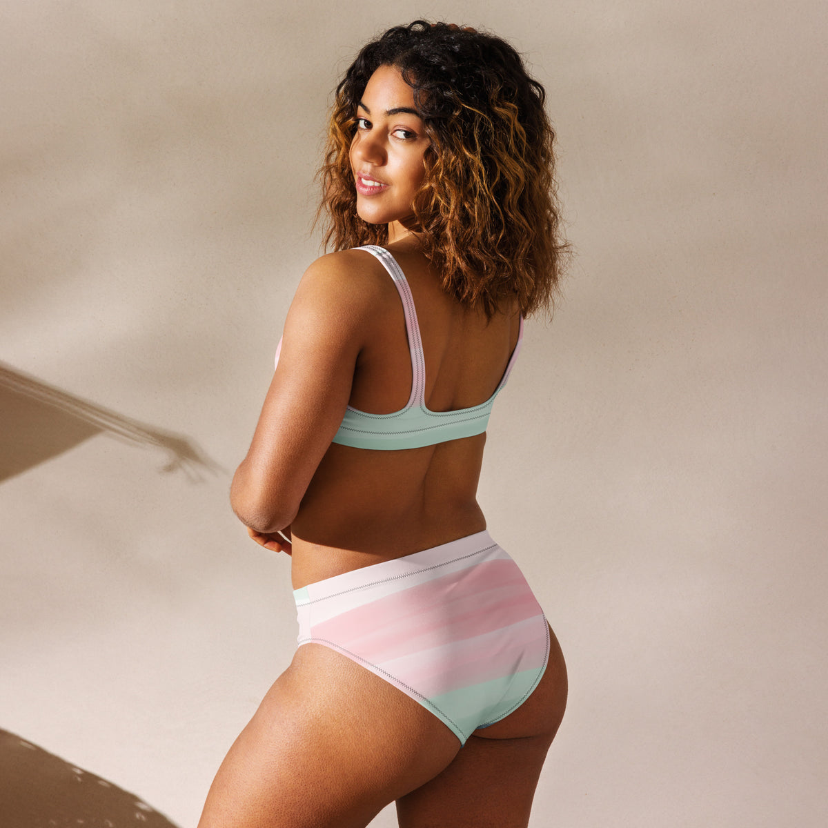 Rear view of woman wearing bikini with design resembling watercolor stripes. Main colors are light-green and pink.
