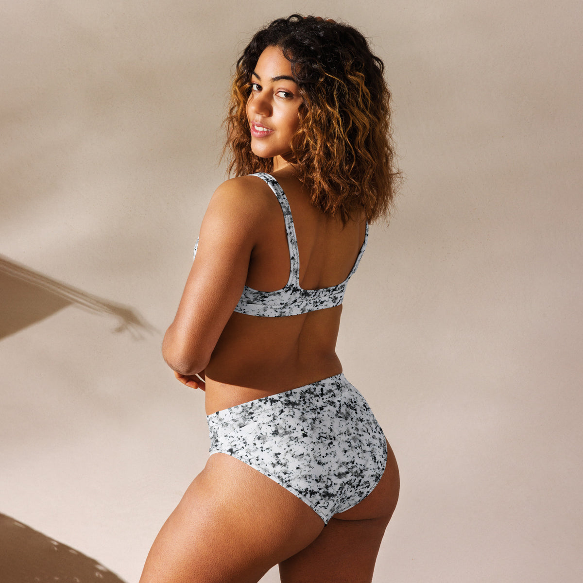 Rear view of woman wearing bikini with pattern of black splotches set on a white background.