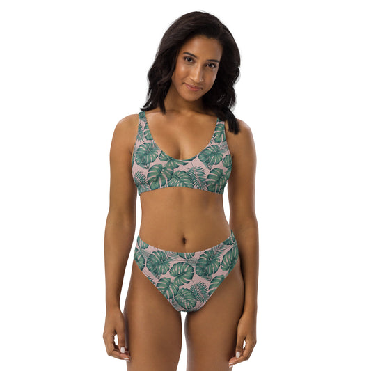 Woman wearing bikini with pattern of green palm leaves set on a pink background.