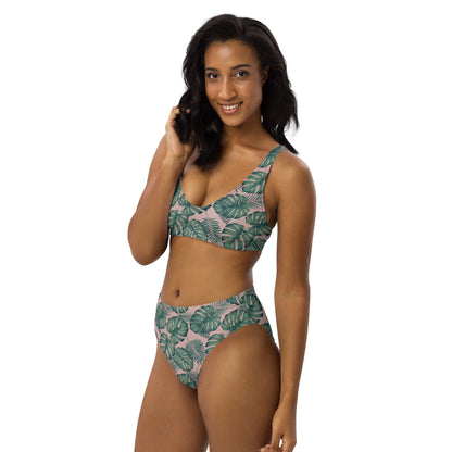Woman wearing bikini with pattern of green palm leaves set on a pink background.
