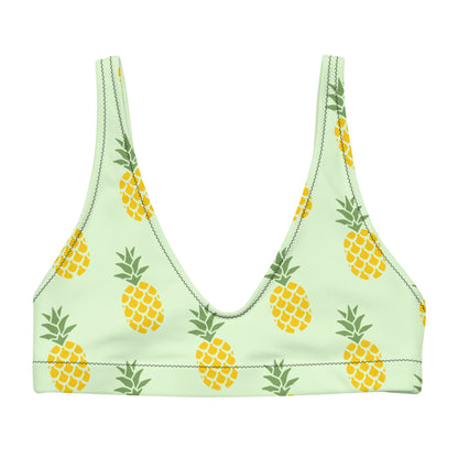 Bikini top with all-over pineapple pattern set on a light-green background.