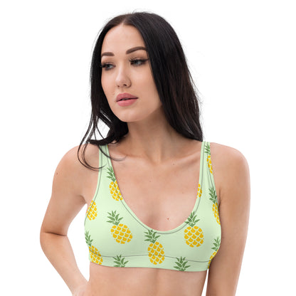 Woman wearing bikini top with all-over pineapple pattern set on a light-green background.