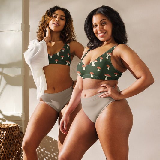 Two women, each wearing bikini top with pattern of mushrooms set on a green background.