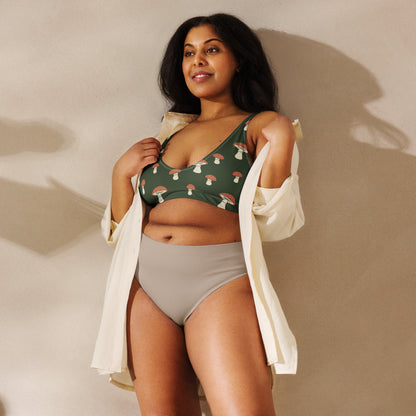 Woman wearing bikini top with pattern of mushrooms set on a green background.