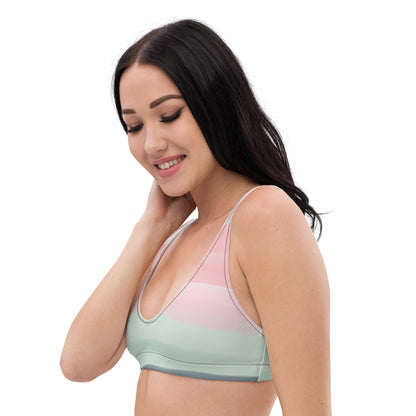 Woman wearing bikini top with design resembling watercolor. Dominant colors are pink and light green.