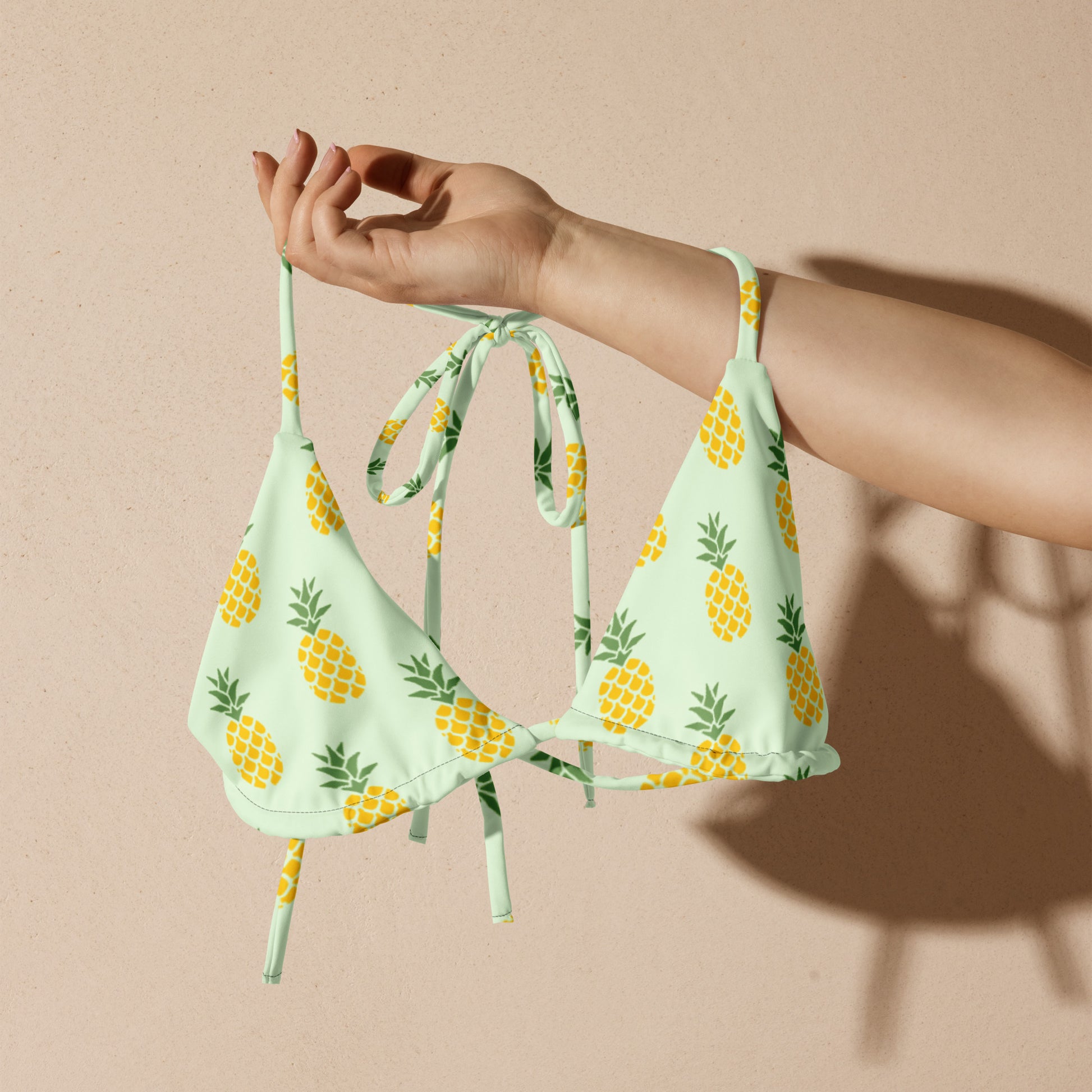 Woman holding a light-green bikini top with all-over pineapple pattern.