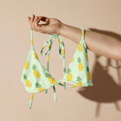 Woman holding a light-green bikini top with all-over pineapple pattern.