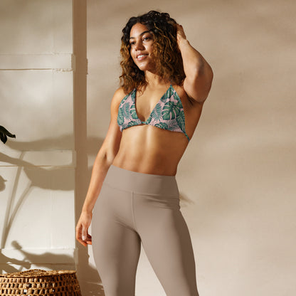 Woman wearing bikini top with pattern of green palm leaves set on a pink background.