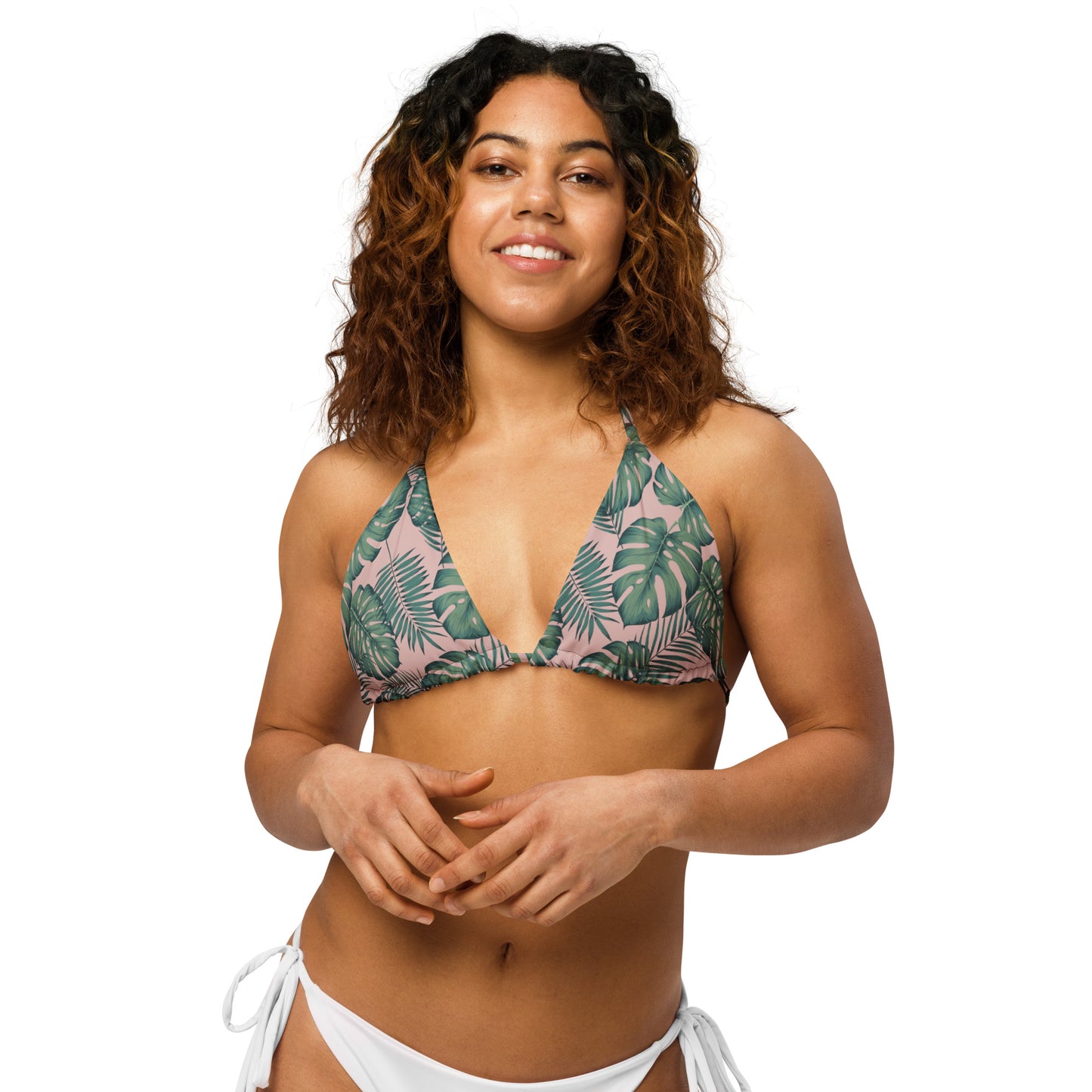 Woman wearing bikini top with pattern of green palm leaves set on a pink background.