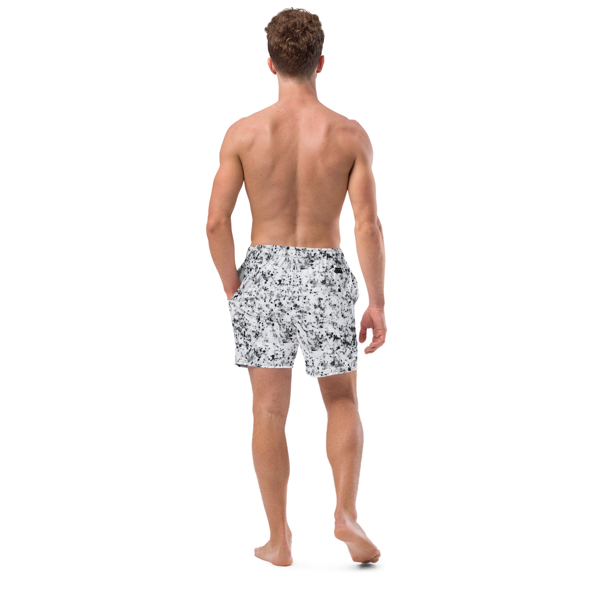 Rear view of man wearing swim trunks with pattern of black splotches on a white background.