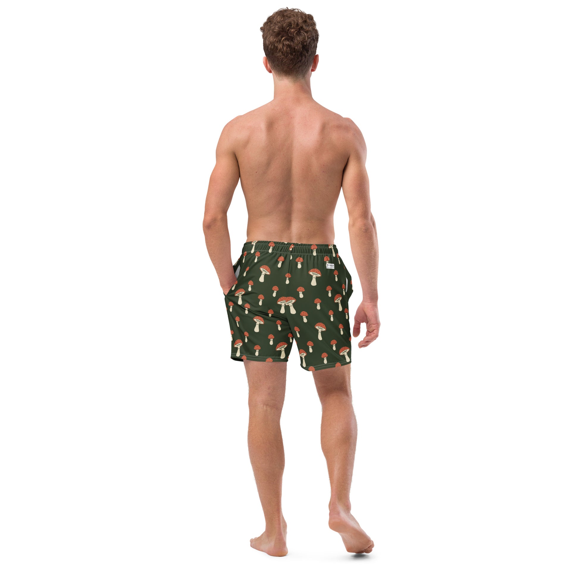 Rear view of man wearing swim trunks with pattern of mushrooms on a green background.