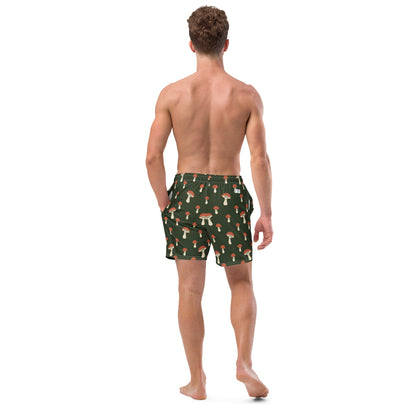 Rear view of man wearing swim trunks with pattern of mushrooms on a green background.