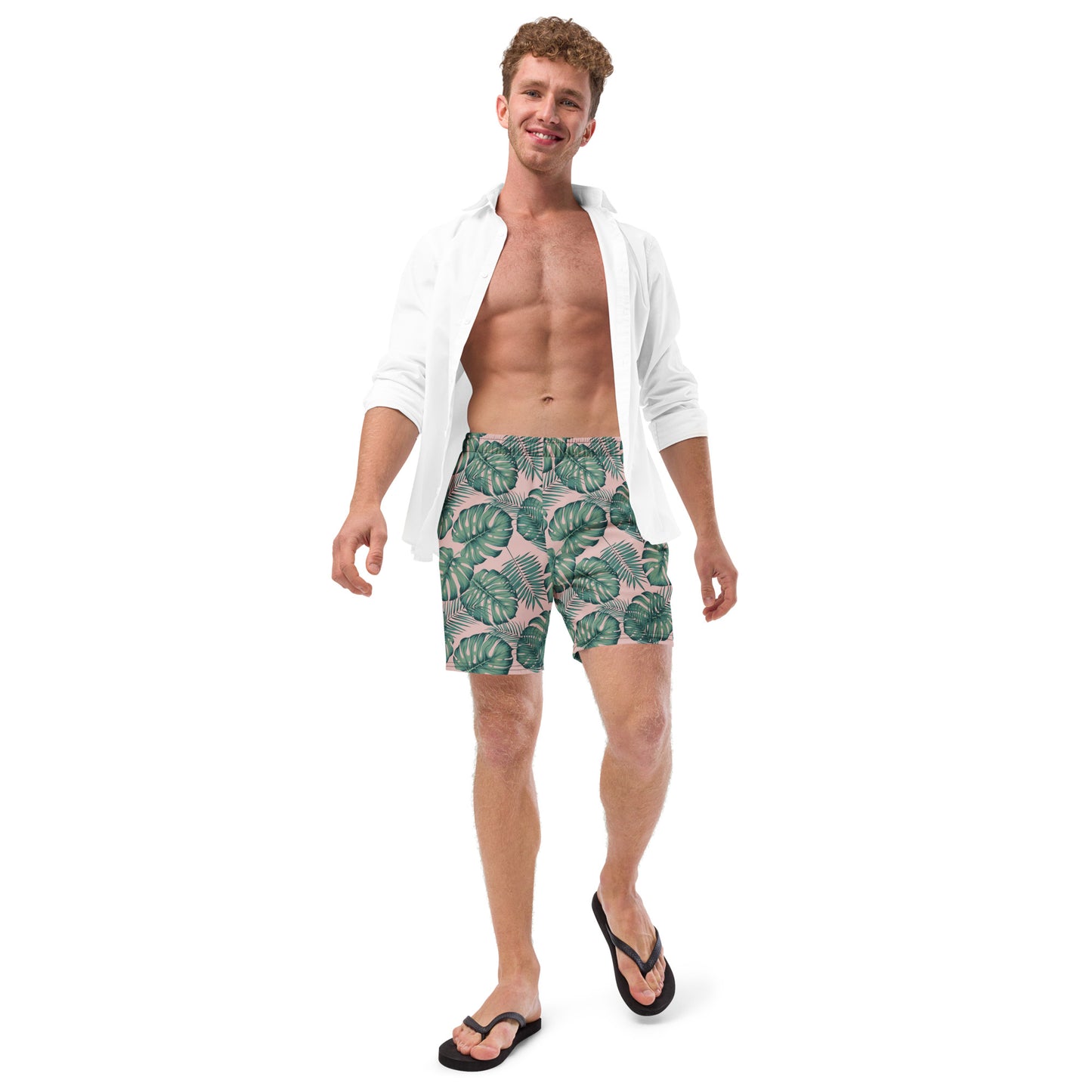Man wearing swim trunks with pattern of green palm leaves set on a pink background.