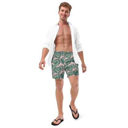 Man wearing swim trunks with pattern of green palm leaves set on a pink background.