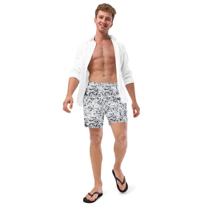 Man wearing swim trunks with pattern of black splotches on a white background.