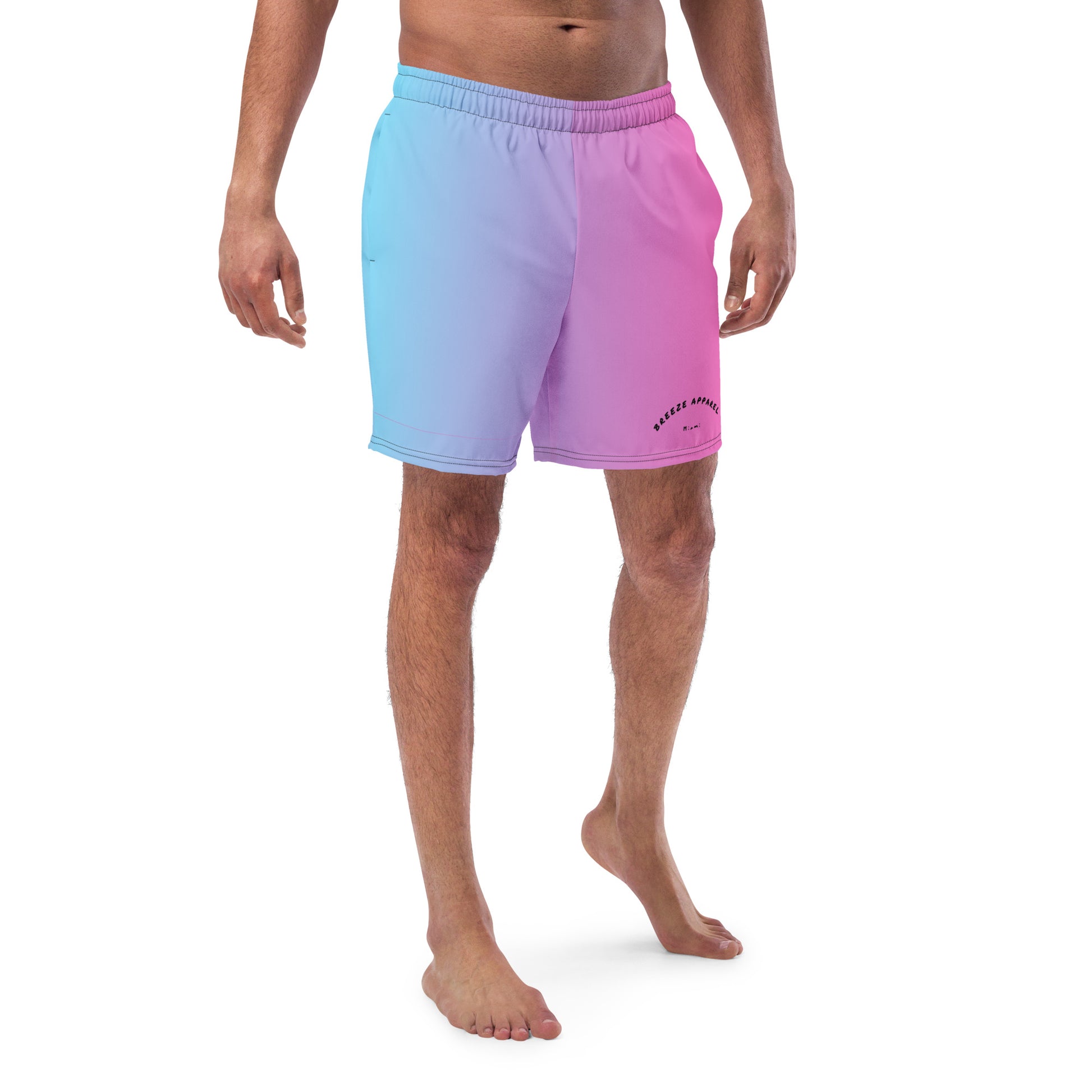 Man wearing swim trunks with a light-blue-to-pink design and a black 'Breeze Apparel Miami' word logo on the bottom-left knee