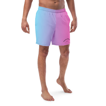 Man wearing swim trunks with a light-blue-to-pink design and a black 'Breeze Apparel Miami' word logo on the bottom-left knee