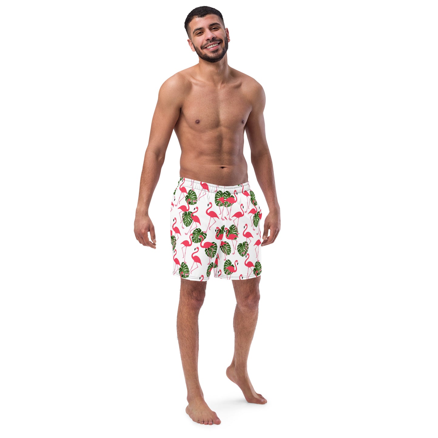 Man wearing swim trunks with pattern of pink flamingos and green leaves set on a white background.
