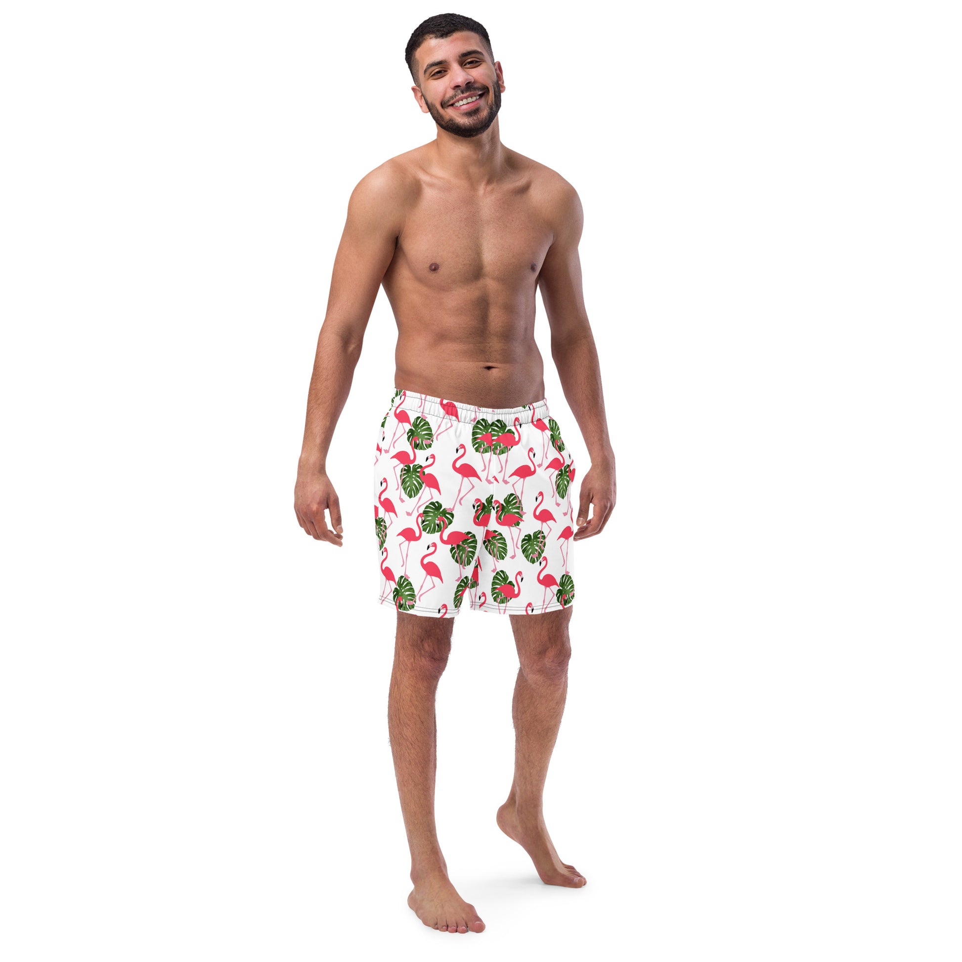 Man wearing swim trunks with pattern of pink flamingos and green leaves set on a white background.