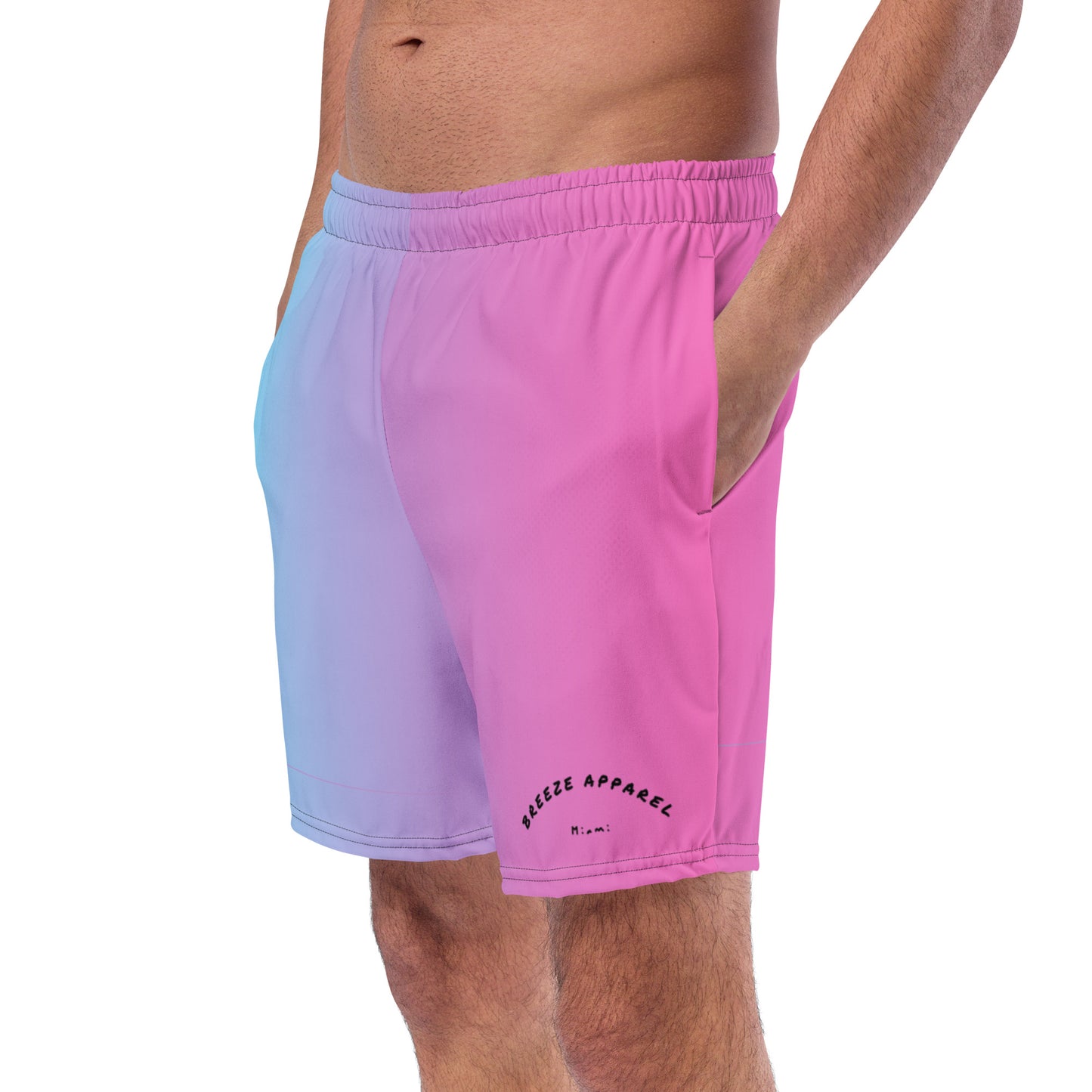 Man wearing swim trunks with a light-blue-to-pink design and a black 'Breeze Apparel Miami' word logo on the bottom-left knee