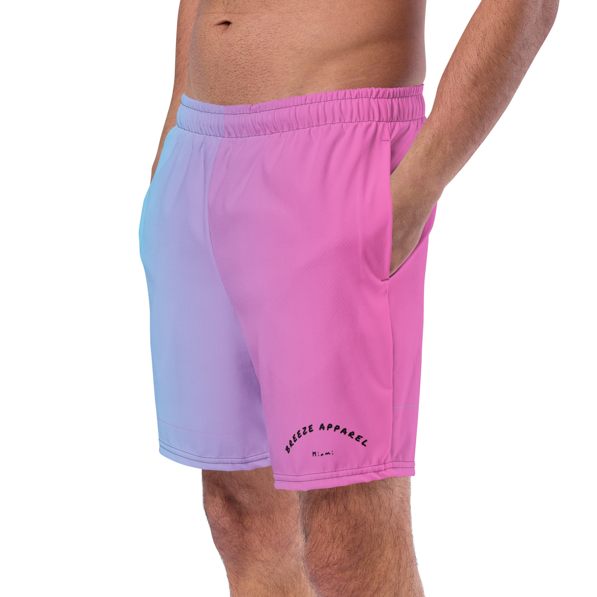 Man wearing swim trunks with a light-blue-to-pink design and a black 'Breeze Apparel Miami' word logo on the bottom-left knee
