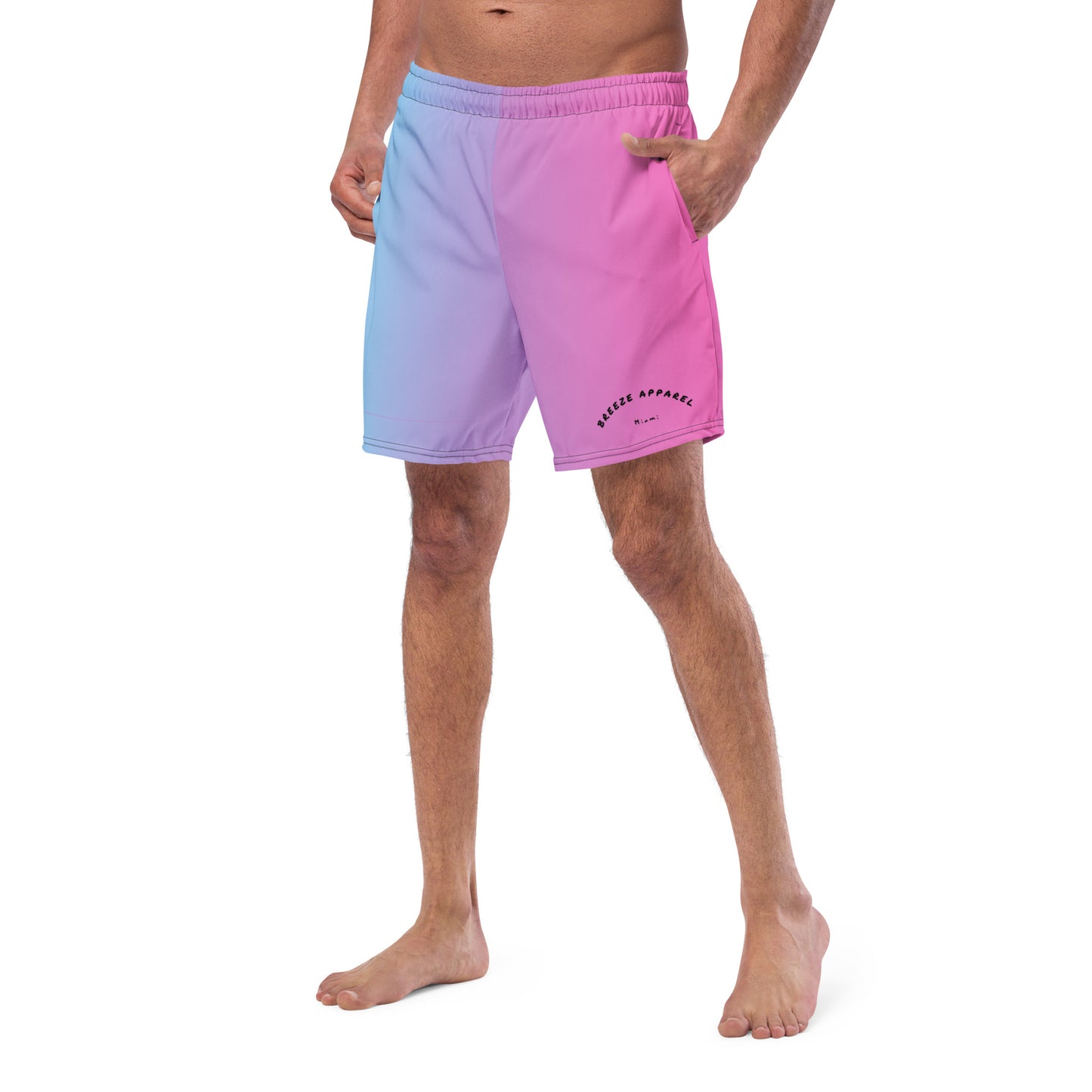 Man wearing swim trunks with a light-blue-to-pink design and a black 'Breeze Apparel Miami' word logo on the bottom-left knee